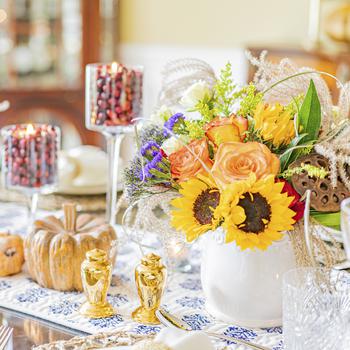 A colorful Thanksgiving harvest tablescape using fall colors and tall glass candlesticks. Ross, an entertaining and food blogger, filled the candlesticks with fresh cranberries and tea lights for a creative lighting idea. Supermarket flowers and simple candles are really all you need to create ambience at a dinner party. 