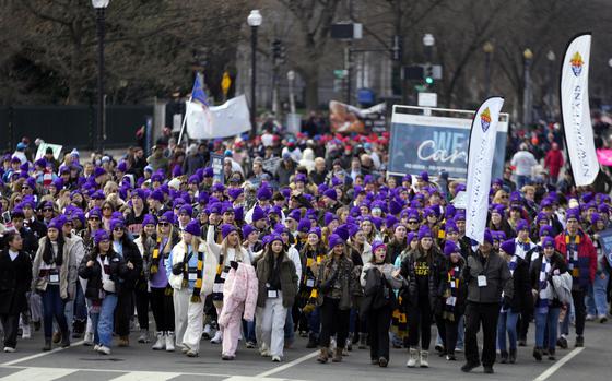 A large group of people wearing purple hats marches down a street.