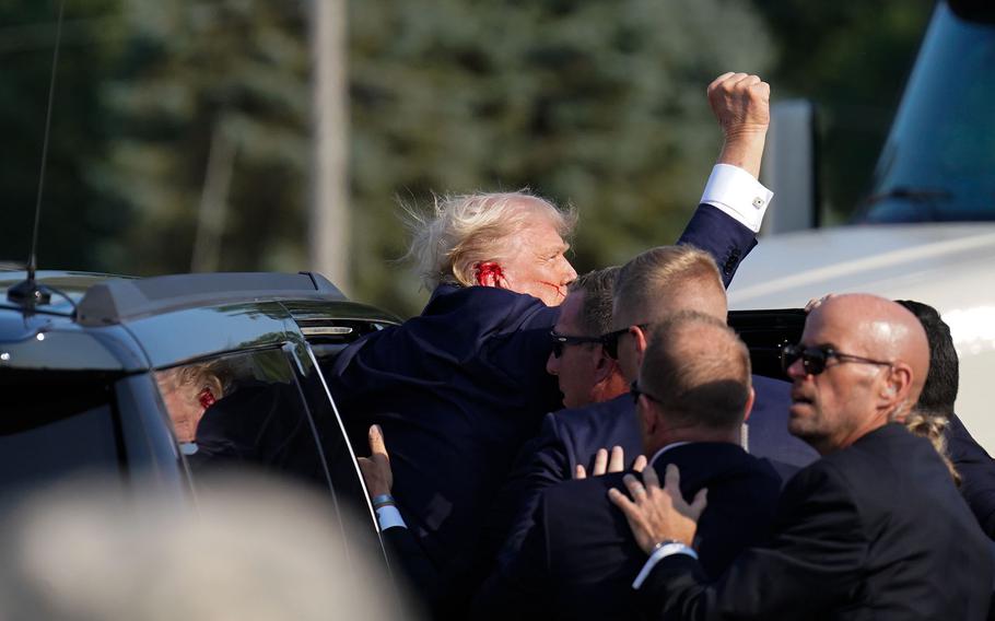 Trump raises his arm as he’s helped into a vehicle after a bullet grazed him during a campaign rally in Butler, Pa., on July 13, 2024.