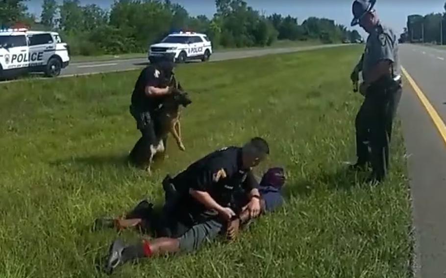 This screenshot from an Ohio State Highway Patrol body-cam video shows a police dog attacking a man whose hands are raised on July 4, 2023.