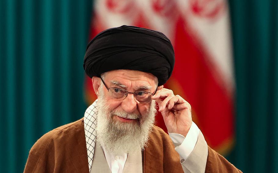 A closeup of Ali Khamenei as he adjusts his glasses with one hand.