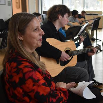 A teacher sits next to students with guitars.