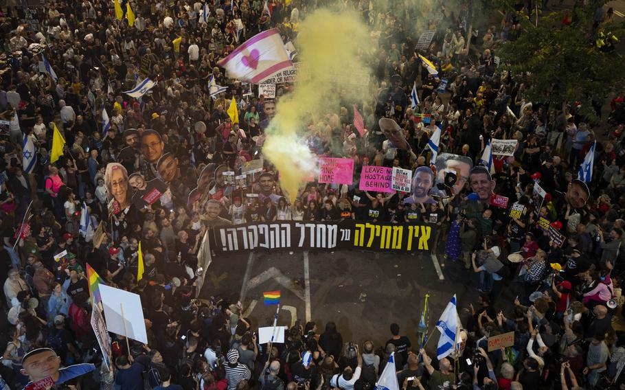 A large crowd, carrying signs, with yellow smoke rising from the center.