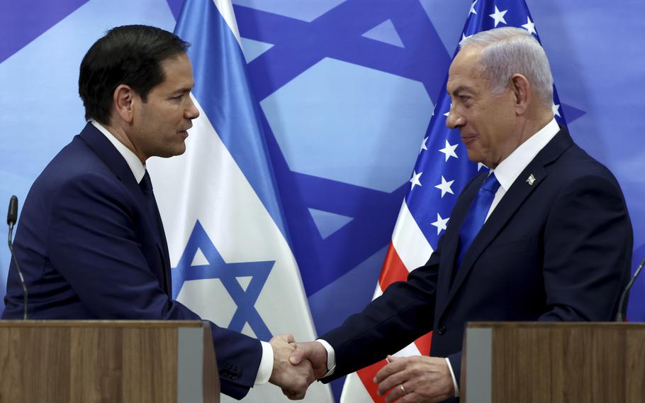 Marco Rubio and Benjamin Netanyahu shake hands with Israeli and U.S. flags in the background.