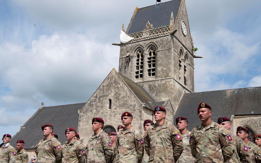 U.S. soldiers attend a ceremony in Sainte-Mère-Église, France, to honor Dwight D. Eisenhower on Monday, June 3, 2024. A paratrooper mannequin hangs from the church behind them to honor the paratroopers who helped liberate the town in 1944 under Eisenhower’s leadership. 