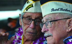 Two elderly men wearing hats and flowered leis speak to each other.