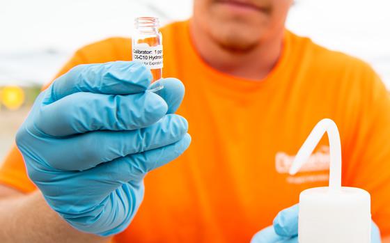 A man in an orange shirt and blue rubber gloves holds up a small vial while testing water samples.