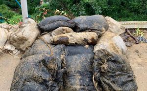 A rusty and corroded looking bomb sits atop black sandbags outside.