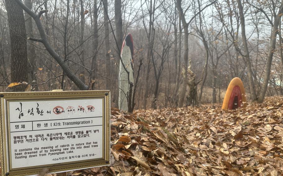 A sign in several languages is in the foreground, with leaves and trees in the background.