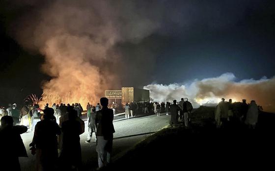 Protesters marching in support of former Pakistani Prime Minister Imran Khan stand on a road at night where bushes are burning, Nov. 24, 2024.