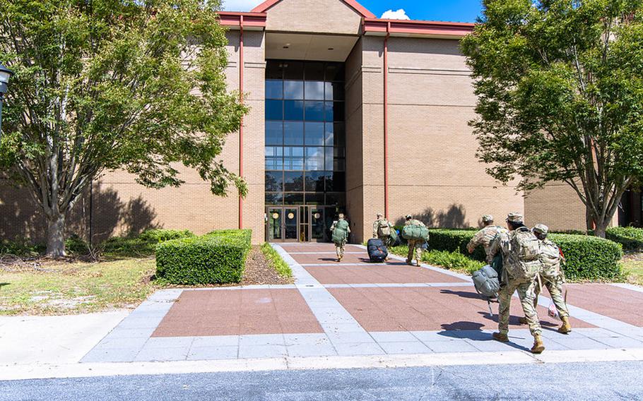 The entrance to a beige building is seen with six soldiers carrying backpacks or luggage walking into it.