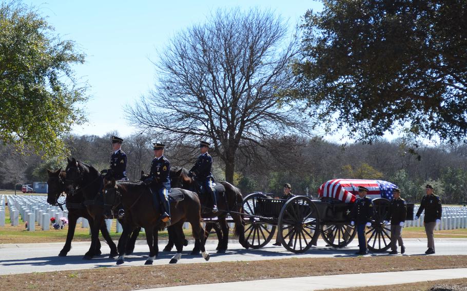 Four soldiers on horses pull a carriage with a casket on it.