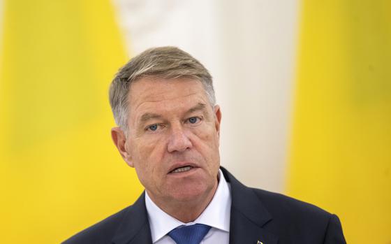 A man in a suit and tie seen from the shoulders up against a yellow and white background.