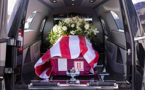 Flowers and the American flag draped over a red casket in the back of a black van.