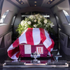 Flowers and the American flag draped over a red casket in the back of a black van.