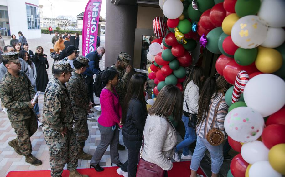 People, some in military uniform, walk on a red carpet through a balloon arch.