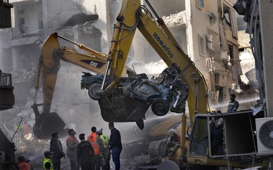 An excavator removes a destroyed car as rescue workers gather at the site of an Israeli airstrike that hit central Beirut, Lebanon, Saturday, Nov. 23, 2024. (AP Photo/Hussein Malla)