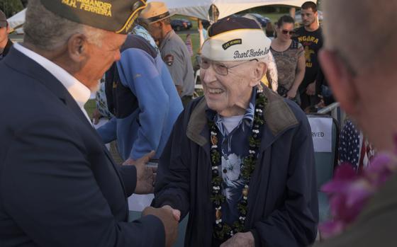 Two elderly men in naval hats shake hands.