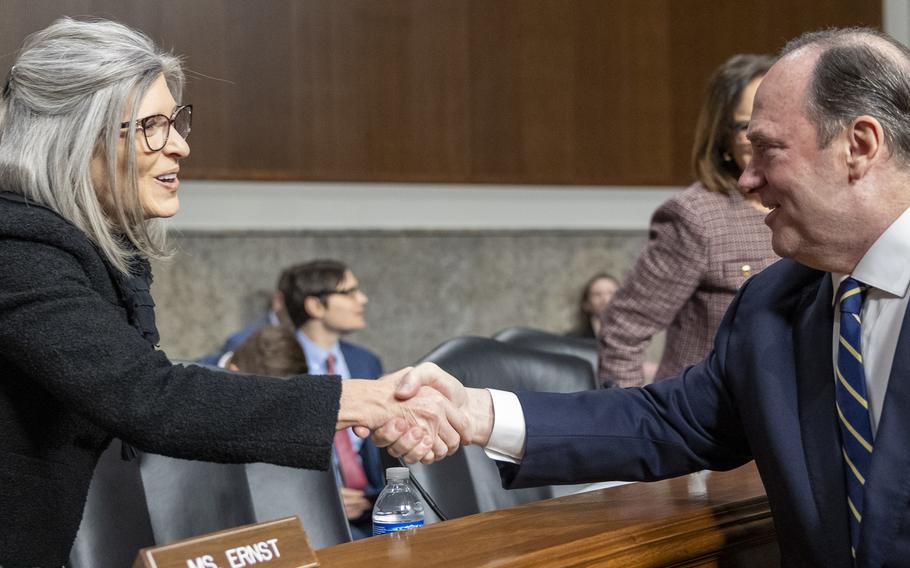 Ernst in a black jacket shakes hands with Phelan, who is wearing a blue suit.