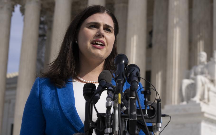 A woman in a suit speaks into a bank of microphones while standing in front of the U.S. Supreme Court building.