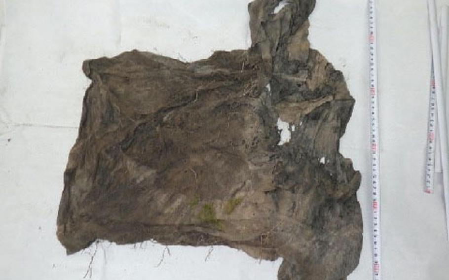 A T-shirt covered in soil and moss is shown.