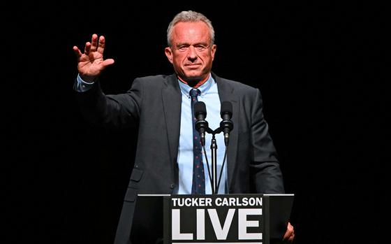 Robert F. Kennedy Jr. raises one hand while standing in front of a podium that reads “Tucker Carlson Live Tour,” Oct. 31, 2024.