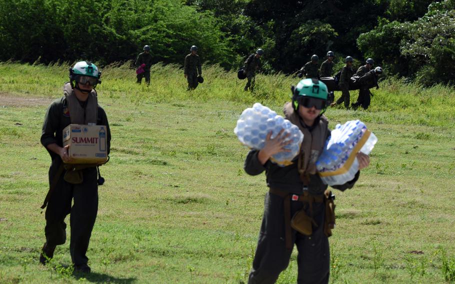 Troops carry cases of water in a field.