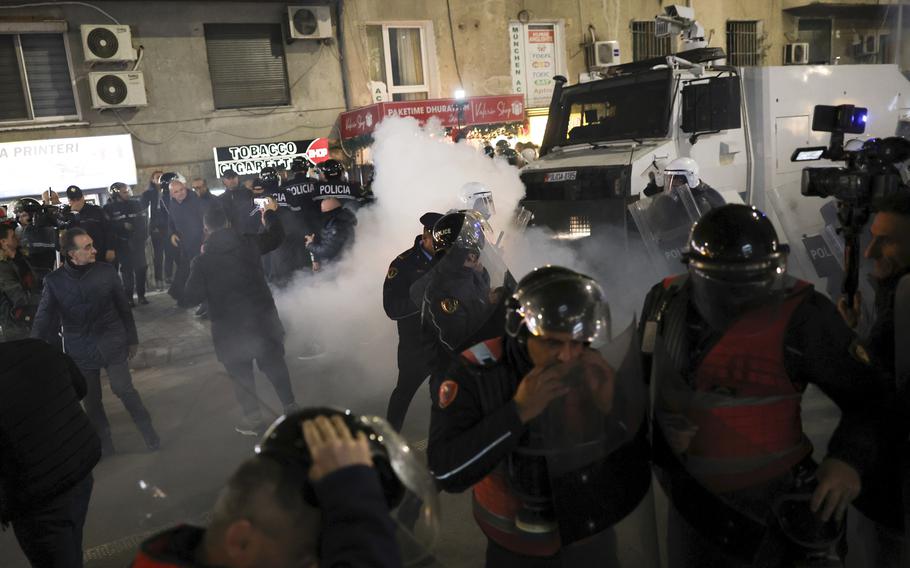 Opposition Supporters and riot police run out of a gas canister thrown by Albania’s police during a protest