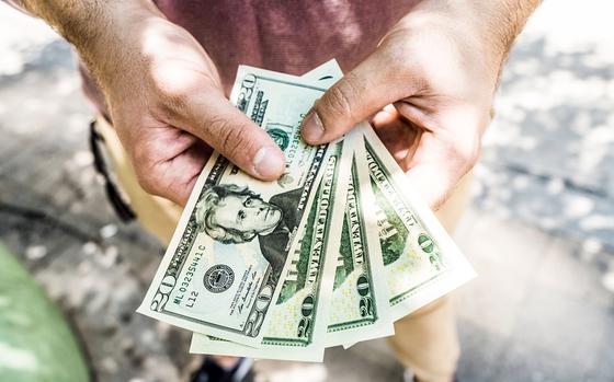 A man holds out four 20 dollar bills in his hands.