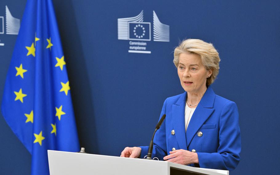 A woman in a blue suit at a podium near the EU flag.