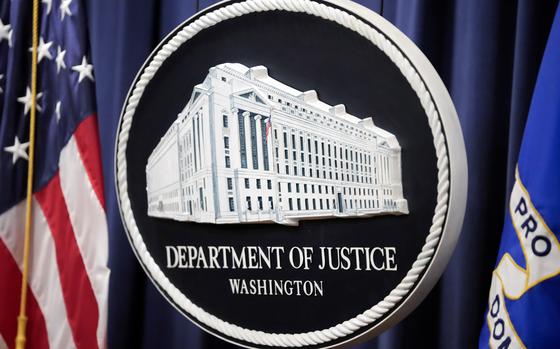 The Justice Department logo is seen in front of a blue backdrop and a U.S. flag.