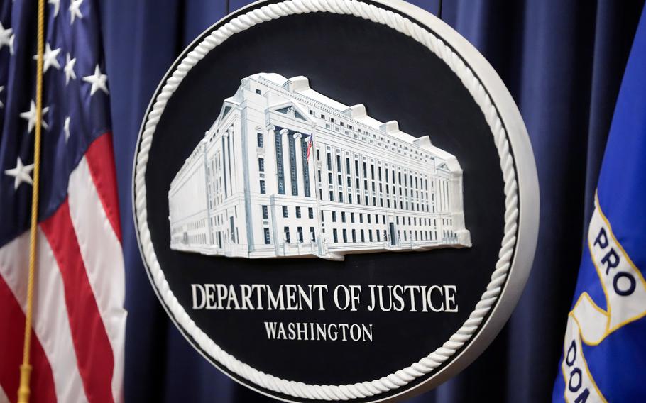 The Justice Department logo is seen in front of a blue backdrop and a U.S. flag.