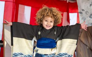 A young boy with curly blonde hair holds his arms outstretched while wearing a kimono.