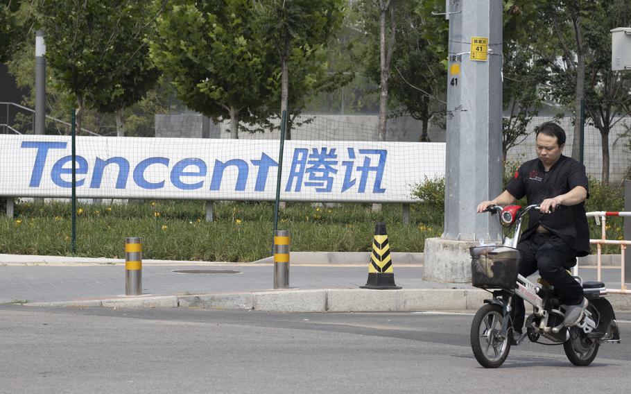 A man in Beijing bicycles past a sign reading Tencent. 