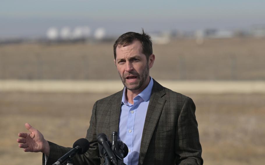 Jason Crow stands at a podium with microphones outside Buckley Space Force Base.