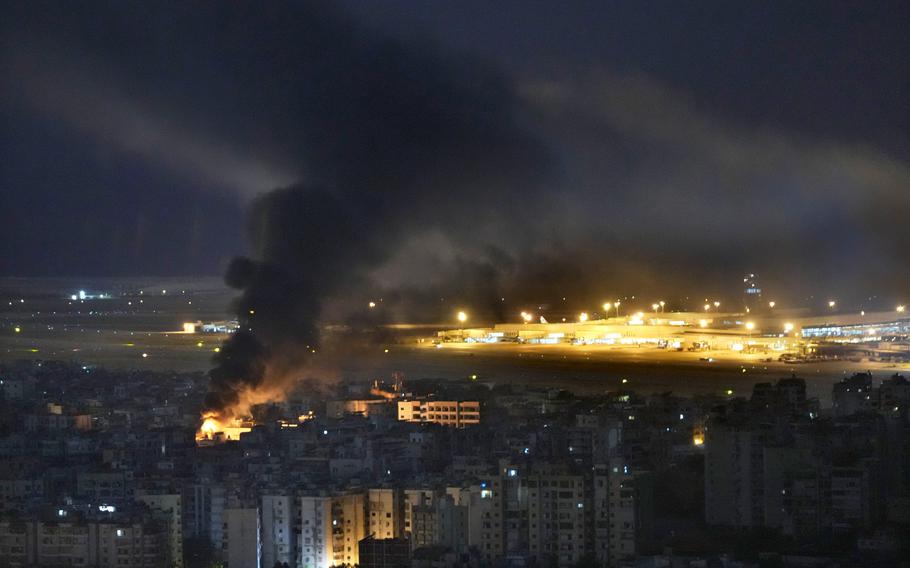 Flames rise from the city in front of an airport.