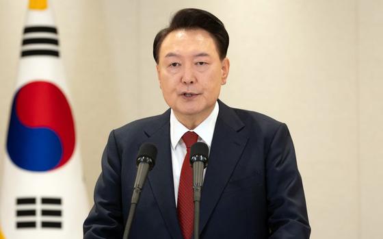 South Korean President Yoon Suk Yeol speaks into a microphone while standing in front of a South Korean flag.