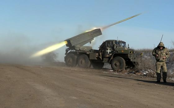 A Ukrainian service member next to a rocket launcher turns away as the launcher fires.