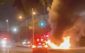 A police car is parked near a car engulfed in flames. 