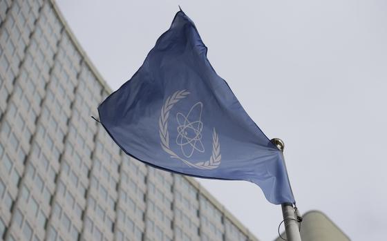 The blue flag of the International Atomic Energy Agency, seen from below, flies in front of its headquarters building.