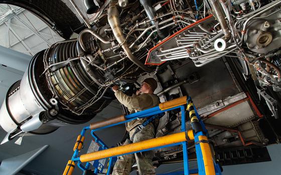 An airman in military uniform inspects and aircraft engine while standing on a raised platform.