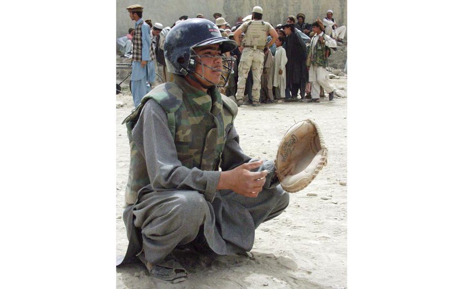 An Afghan boy, wearing a flak vest for protection,  gets ready to take a few practice pitches during a baseball game in Orgun-e, Afghanistan. 