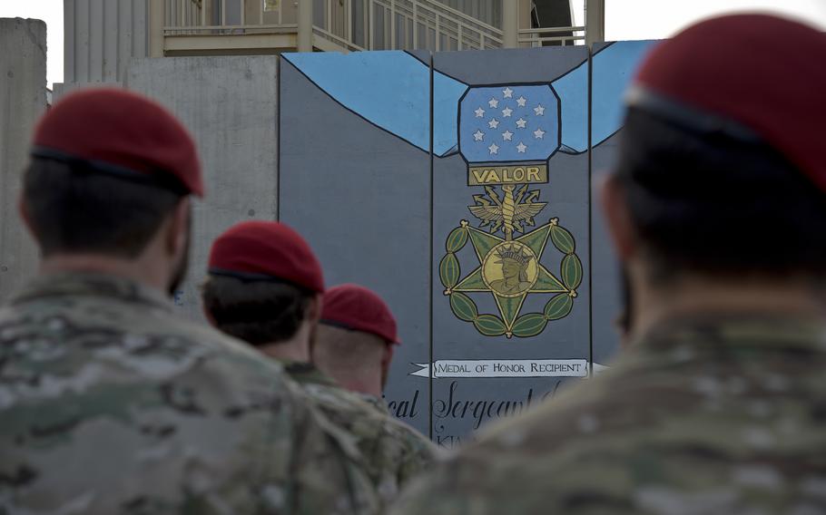 Members of the Special Operations community, wearing red berets, gather in front of a mural.