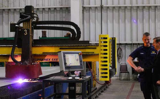 As a plasma cutter carves steel plating that will become part of the future U.S. Coast Guard cutter Pickering, Read Adm. Mike Campbell shakes hands with Bill Bingle, right, a program manager for Austal USA.