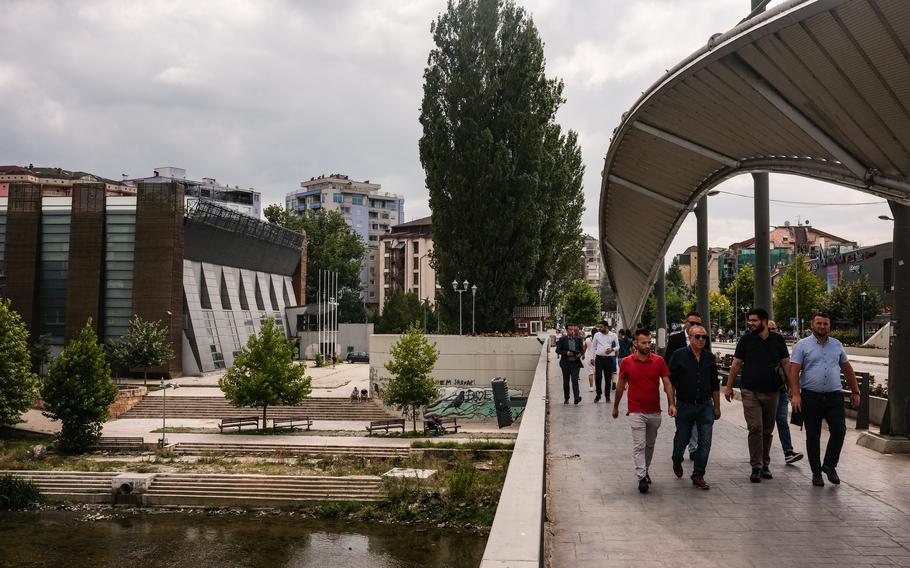 A photo of residents cross a bridge from the south side of the River Ibar.