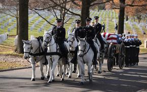 Horses ridden by service members in uniform pull a coffin in a funeral procession at Arlington National Cemetery.