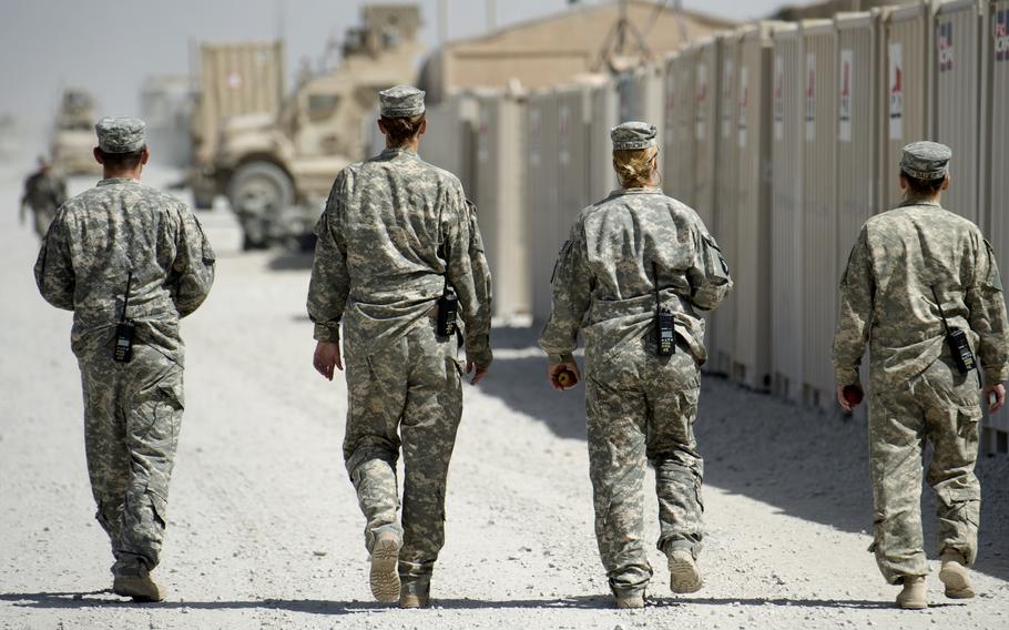 Female soldiers face away from the camera walking on a desert military base. 