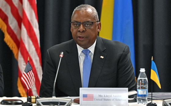 U.S. Defense Secretary Lloyd Austin speaks into a microphone while sitting at a table. 