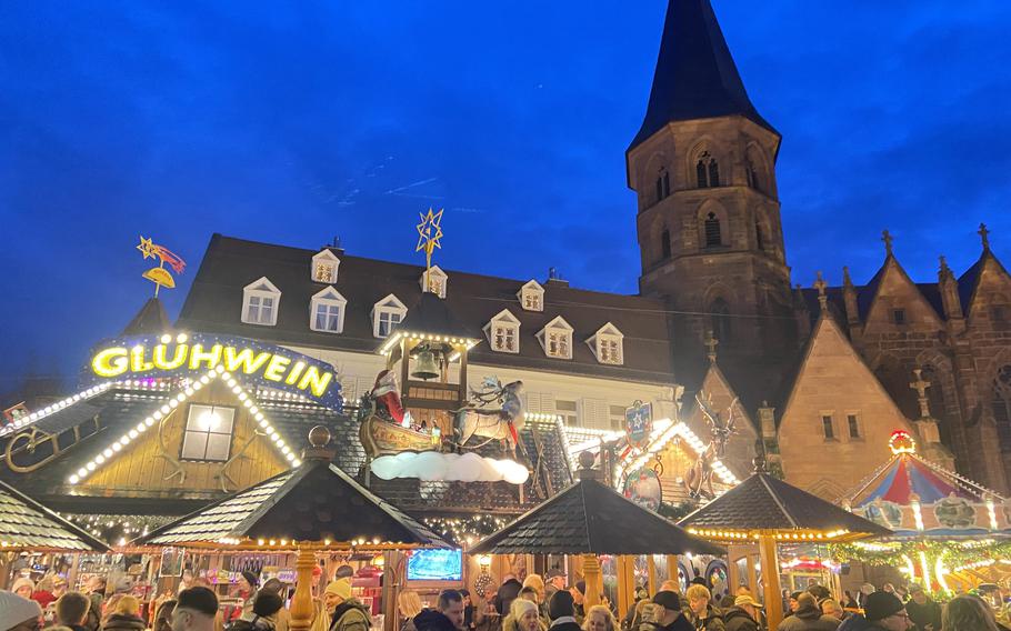 Crowds gather at the Kaiserslautern Christmas market and a lighted sign on one of the stands reads “gluehwine.”