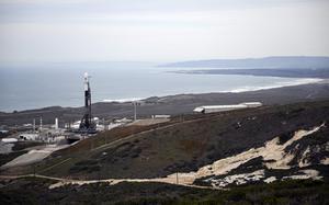 A rocket is on a launch pad beside an ocean coastline.